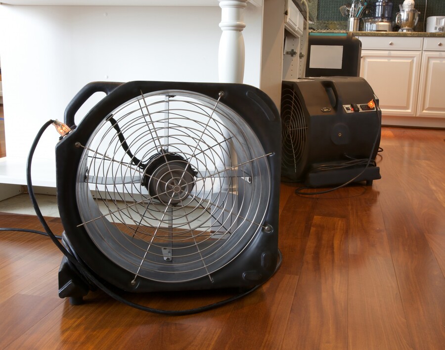 Industrial air movers drying hardwood floor in a kitchen
